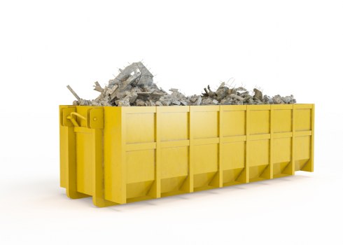 A bright yellow skip bin positioned on a clean, white surface filled with a mixture of grey and white rubble, consisting of broken concrete, bricks, and construction debris. The rectangular skip has a sturdy metal frame with reinforced panels, and the front side features several evenly spaced vertical supports. The rubble inside appears to have rough textures with jagged edges, some fragments leaning against the sides of the bin. The skip is situated outdoors or in a well-lit environment, with no other objects or background details visible. The image captures the process of waste removal typical of professional rubbish disposal services, such as those provided by Business Waste Removal Marylebone, serving local areas with reliable clearance of construction or renovation debris.