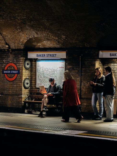 A close-up view of the Baker Street London Underground station sign mounted on a textured brick wall. The sign features a circular red frame with a horizontal blue bar across the center, displaying th